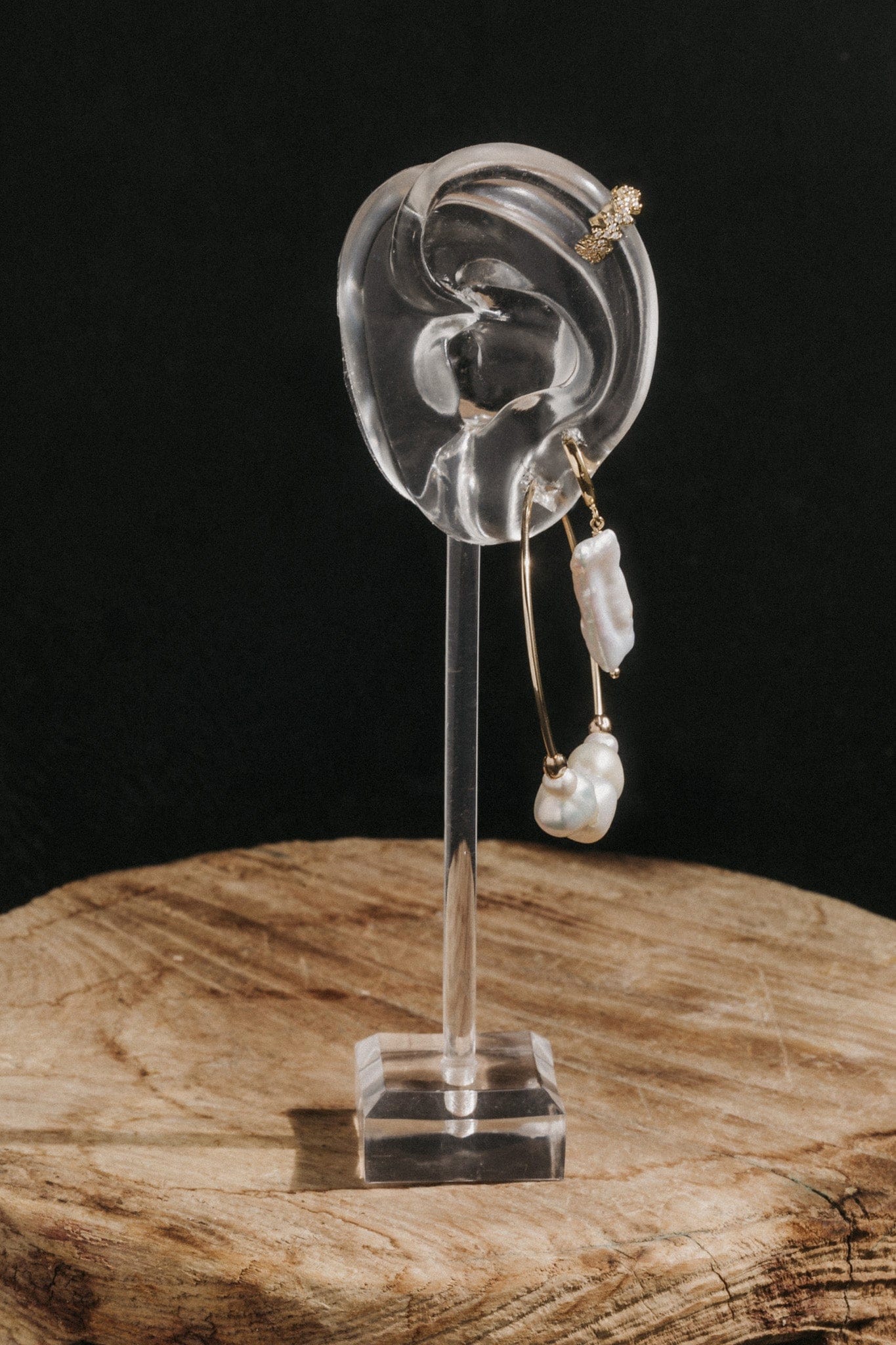Pair of drop earrings with white baroque pearls suspended from gold-tone posts with crystal stone accents, displayed on acryl