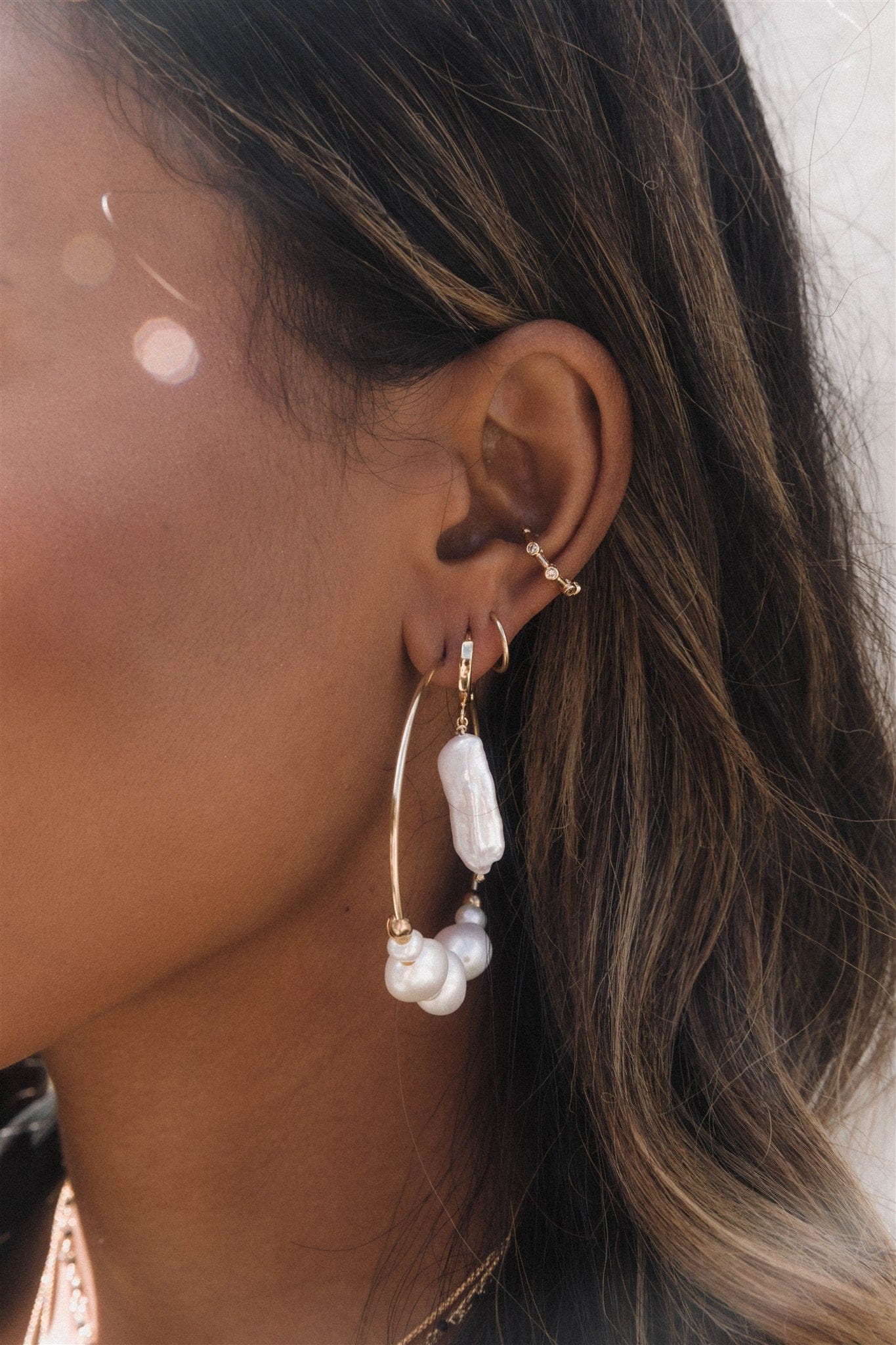 Pearl drop earrings with gold-tone curved posts worn on ear lobe, featuring white baroque pearls and small round pearls suspe