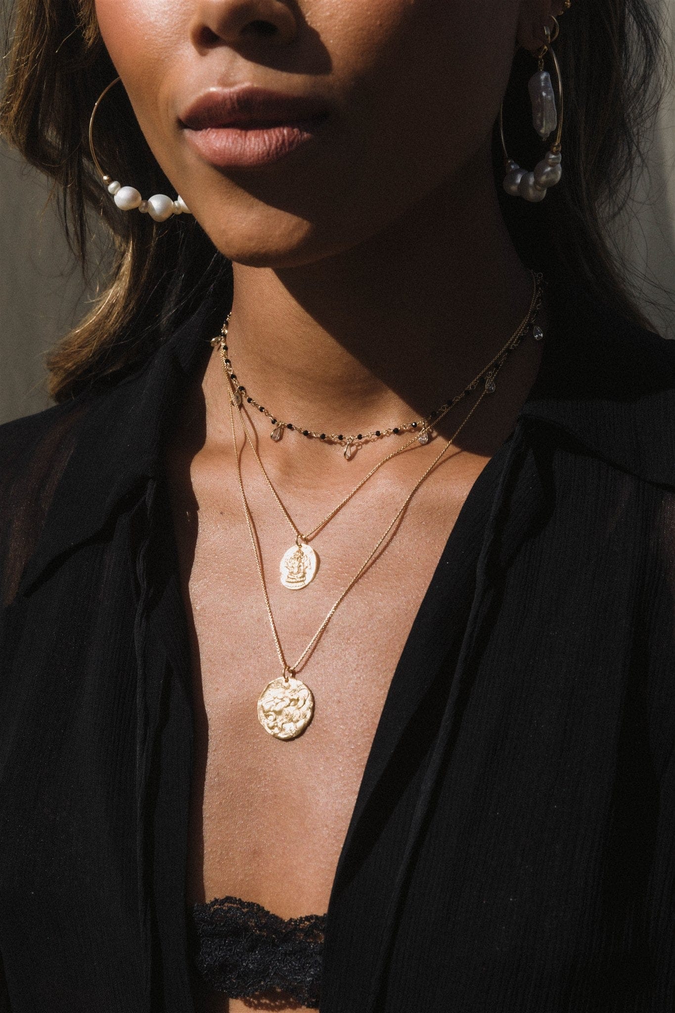 Gold-toned hoop earrings with white and dark pearl accents worn on model with dark hair and black shirt.