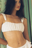White bikini top with ruched fabric and thin shoulder straps on model against green background.