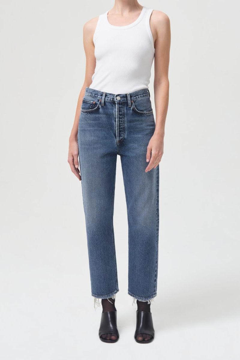 White sleeveless ribbed tank top with crew neckline worn with blue denim jeans.