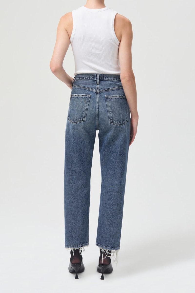 White ribbed sleeveless tank top with crew neckline, styled with blue denim jeans with distressed hems.